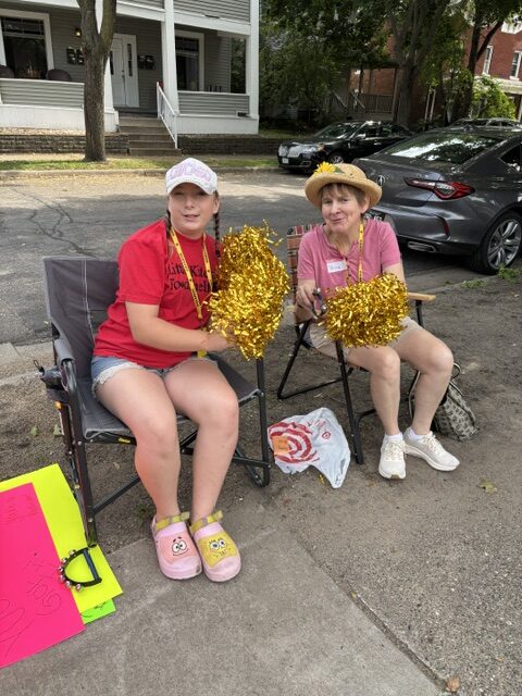 Two people sitting on a bench with gold pom poms